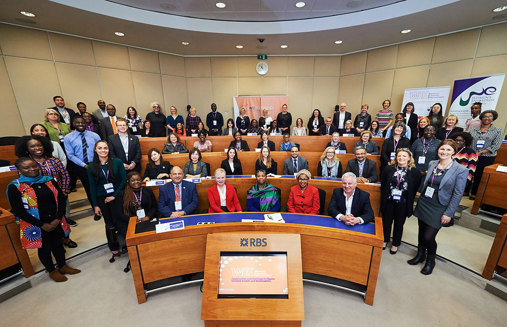A diverse group of individuals gathers in a conference room, seated in wooden benches, showcasing a collaborative and professional atmosphere.