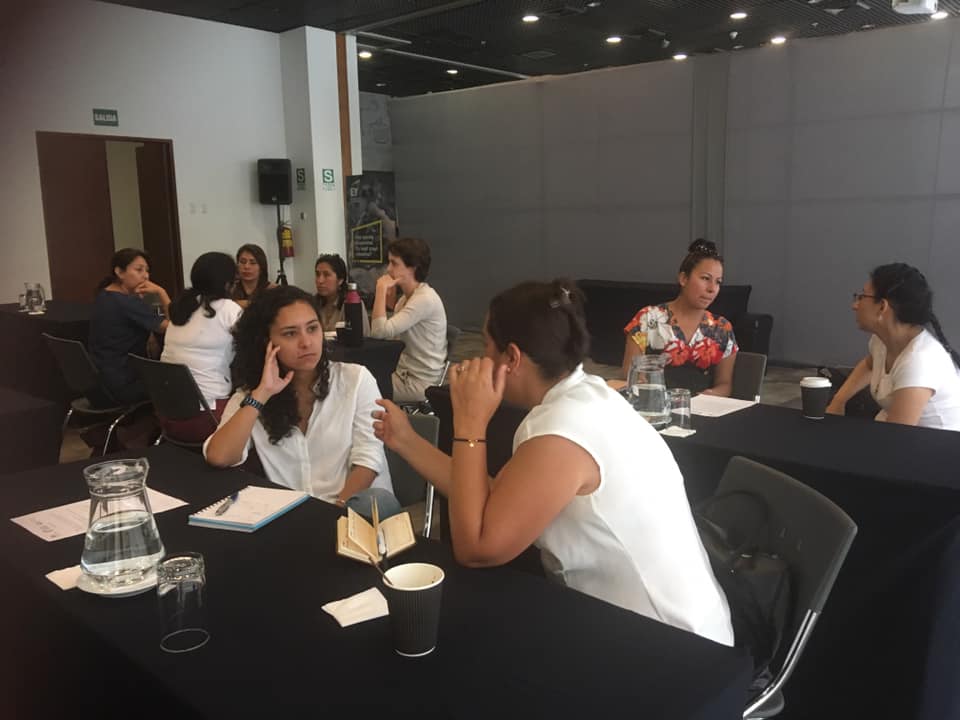 Group of people engaging in discussions at tables in a conference setting, wearing casual white attire.