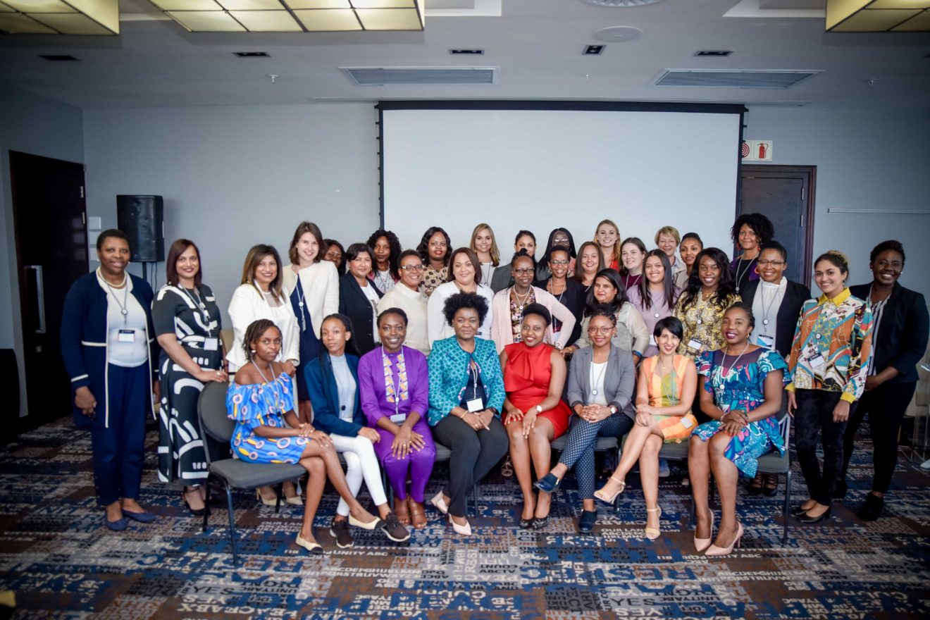 A diverse group of women gathered in a conference room, smiling and posing together for a group photo, showcasing unity and collaboration.