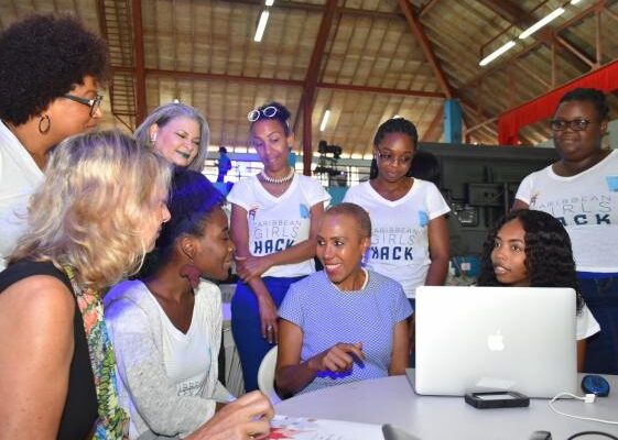 A group of women engaged in a collaborative tech workshop, discussing ideas while working on a laptop, showcasing empowerment and teamwork.
