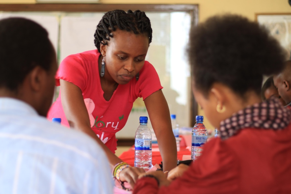 A focused group activity at a table, featuring a woman in a pink shirt engaging with participants surrounded by water bottles.