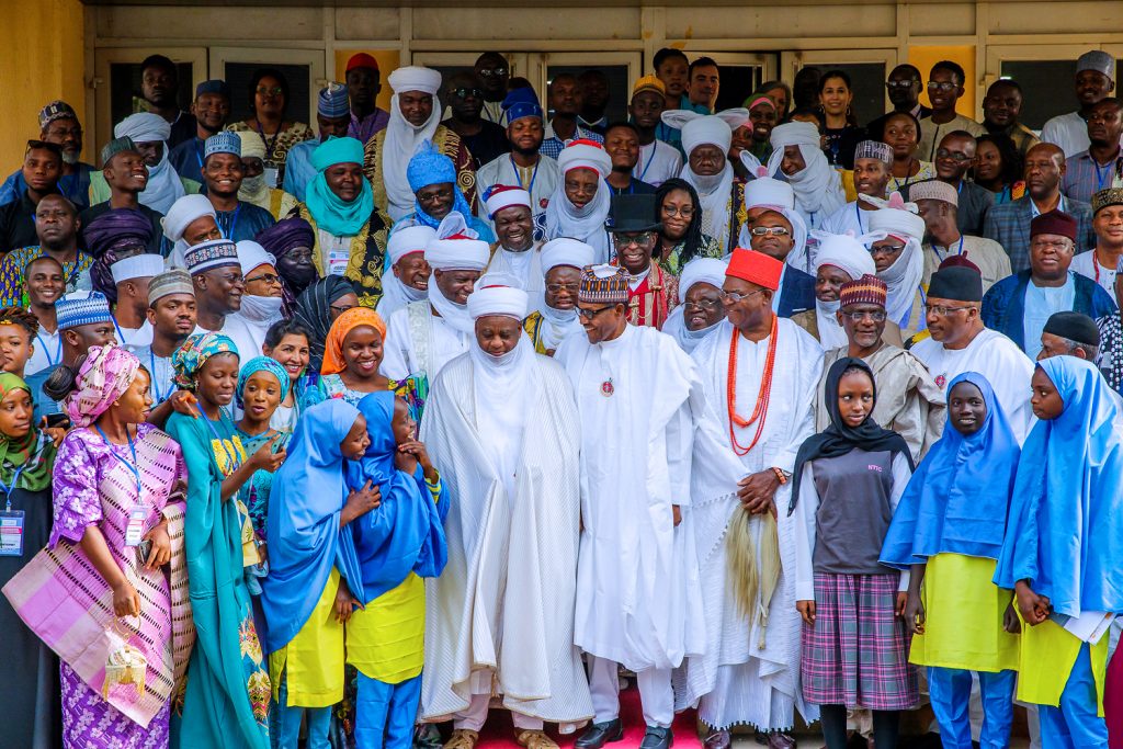 A large group of people in diverse traditional attire, posing together outside, showcasing cultural unity and community engagement.