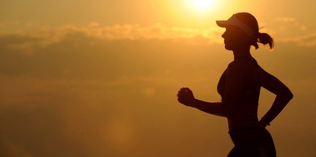 A silhouette of a woman running against a stunning sunset backdrop, with warm colors illuminating the sky.