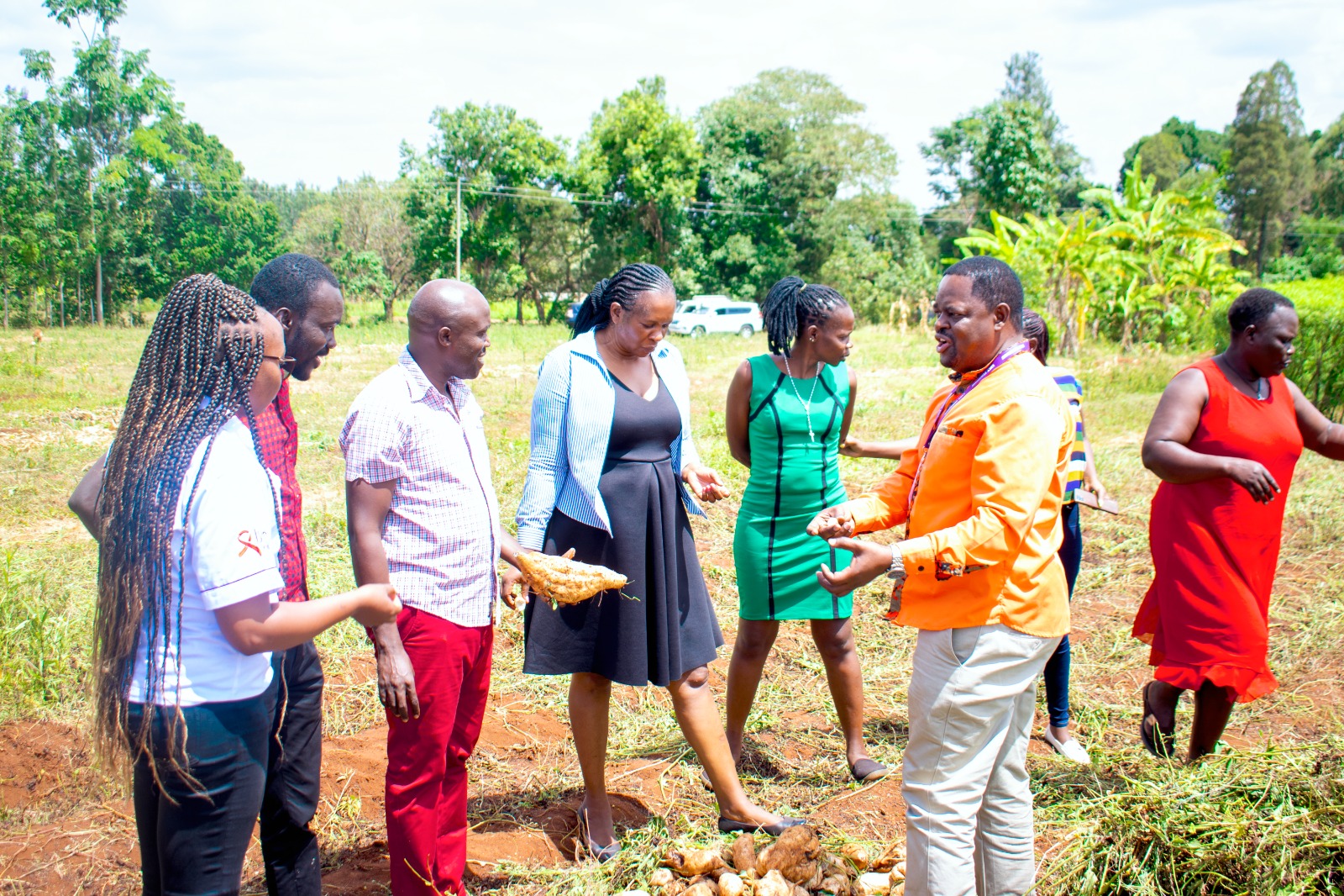 A group of people interacting in a field, engaging in agricultural activities and showcasing harvested produce, with lush greenery in the background.