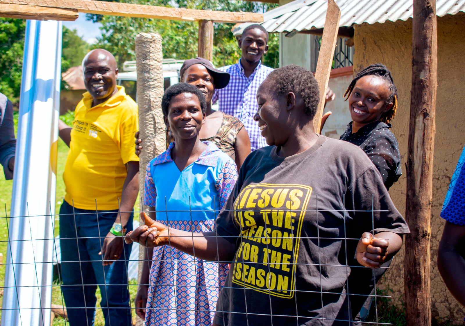 A diverse group of people smiling and engaging in a community activity outdoors, displaying joy and collaboration under bright sunlight.