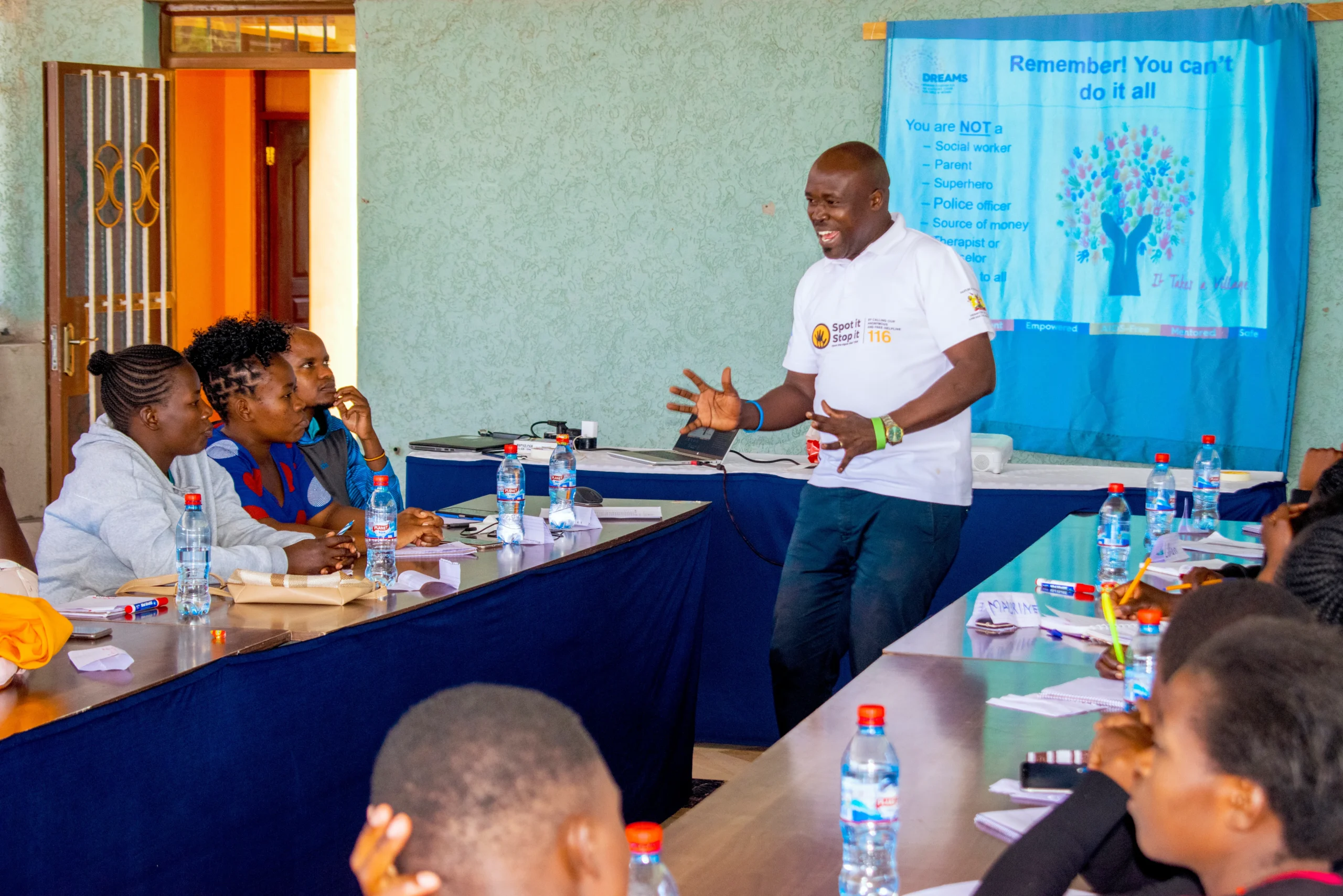 A speaker engages with an audience during a workshop, with participants seated around a table actively listening and interacting.